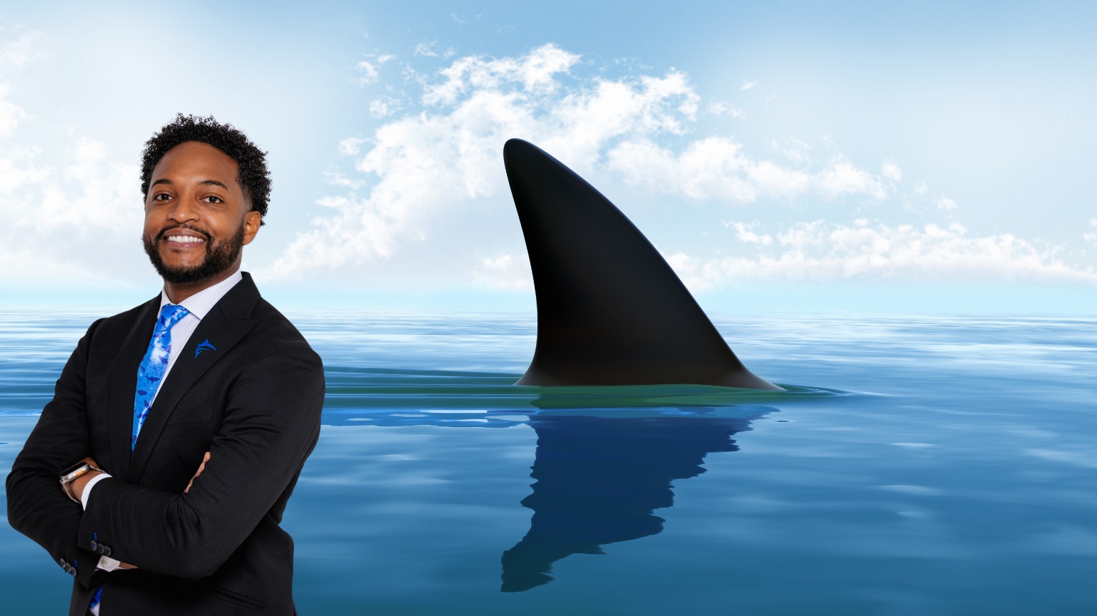Keith Lamar Jr., standing with arms crossed in front of a shark fin at sea